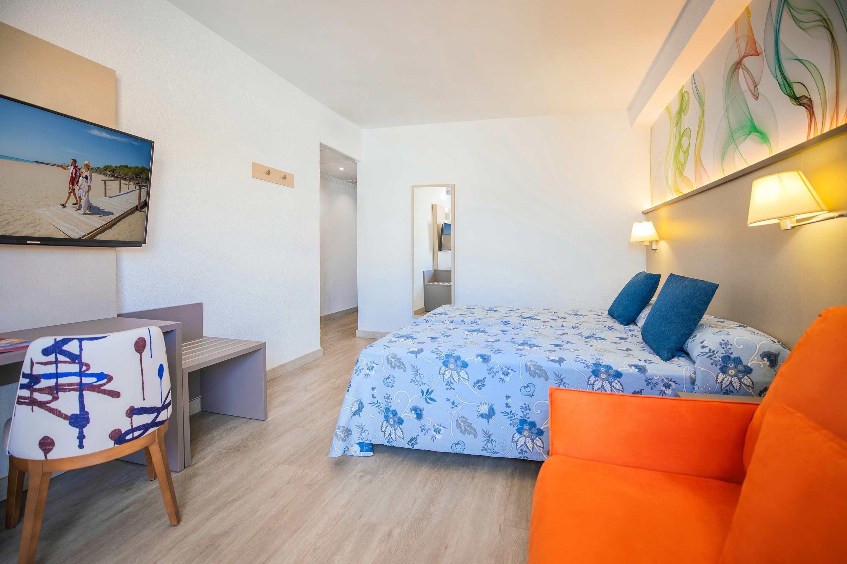 Una habitación de hotel con una cama, un escritorio, una silla y un televisor en la pared.