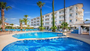 A swimming pool with lounge chairs and palm trees, surrounded by a multi-story hotel building. - Hotel Servigroup Romana (Alcala de Xivert)