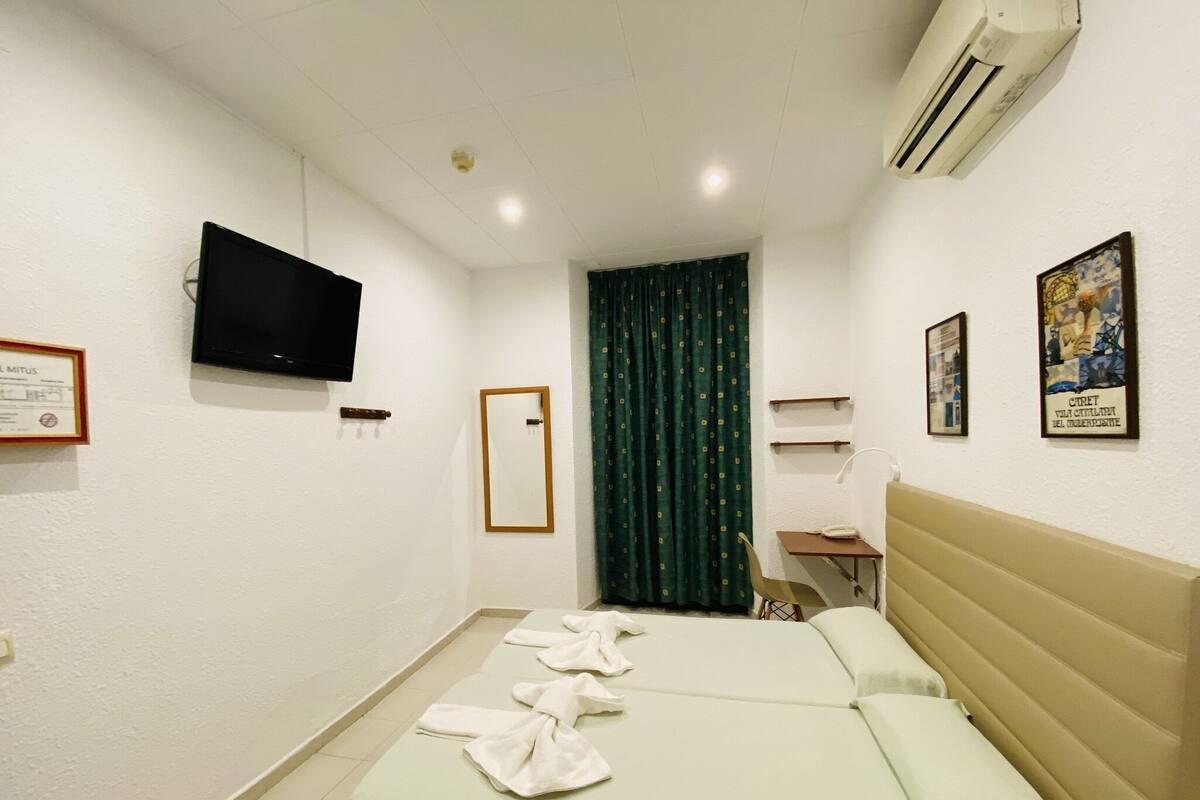 A hotel room with a bed, a desk, a chair, a television, and a window with curtains.