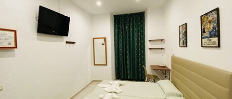 A hotel room with a bed, a desk, a chair, a television, and a window with curtains.