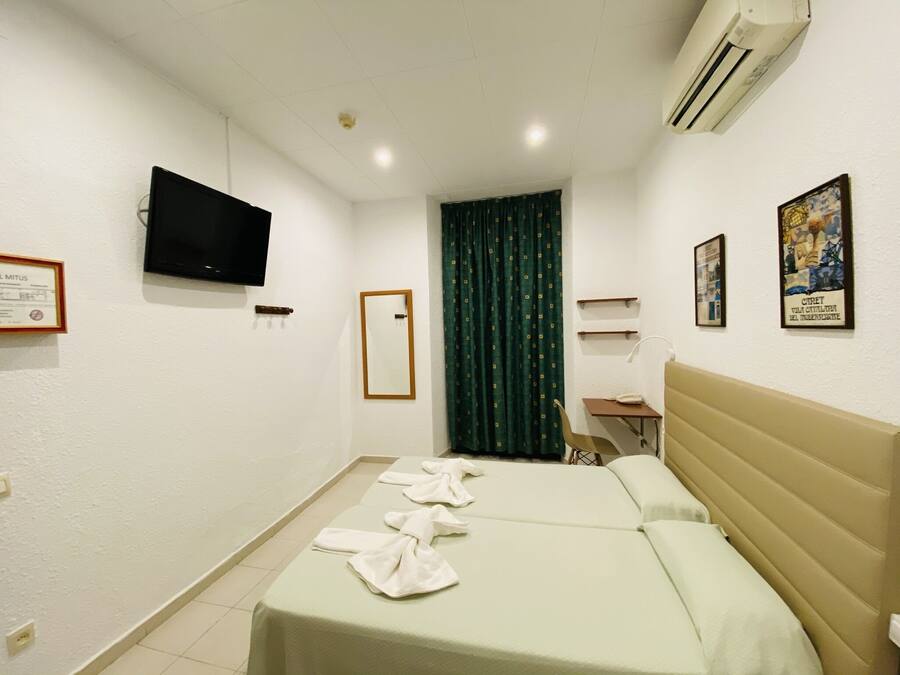 Habitación de hotel con cama, escritorio, silla, televisor y ventana con cortinas.