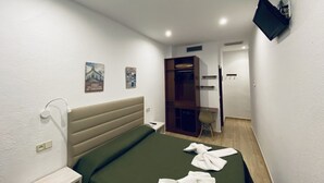 Ein Hotelzimmer mit einem Bett, einem Nachttisch, einem an der Wand befestigten Fernseher und einem Kleiderschrank.