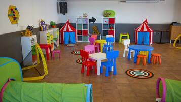 Children can play and explore in this vibrant playroom with tables, chairs, play tents, and storage units.