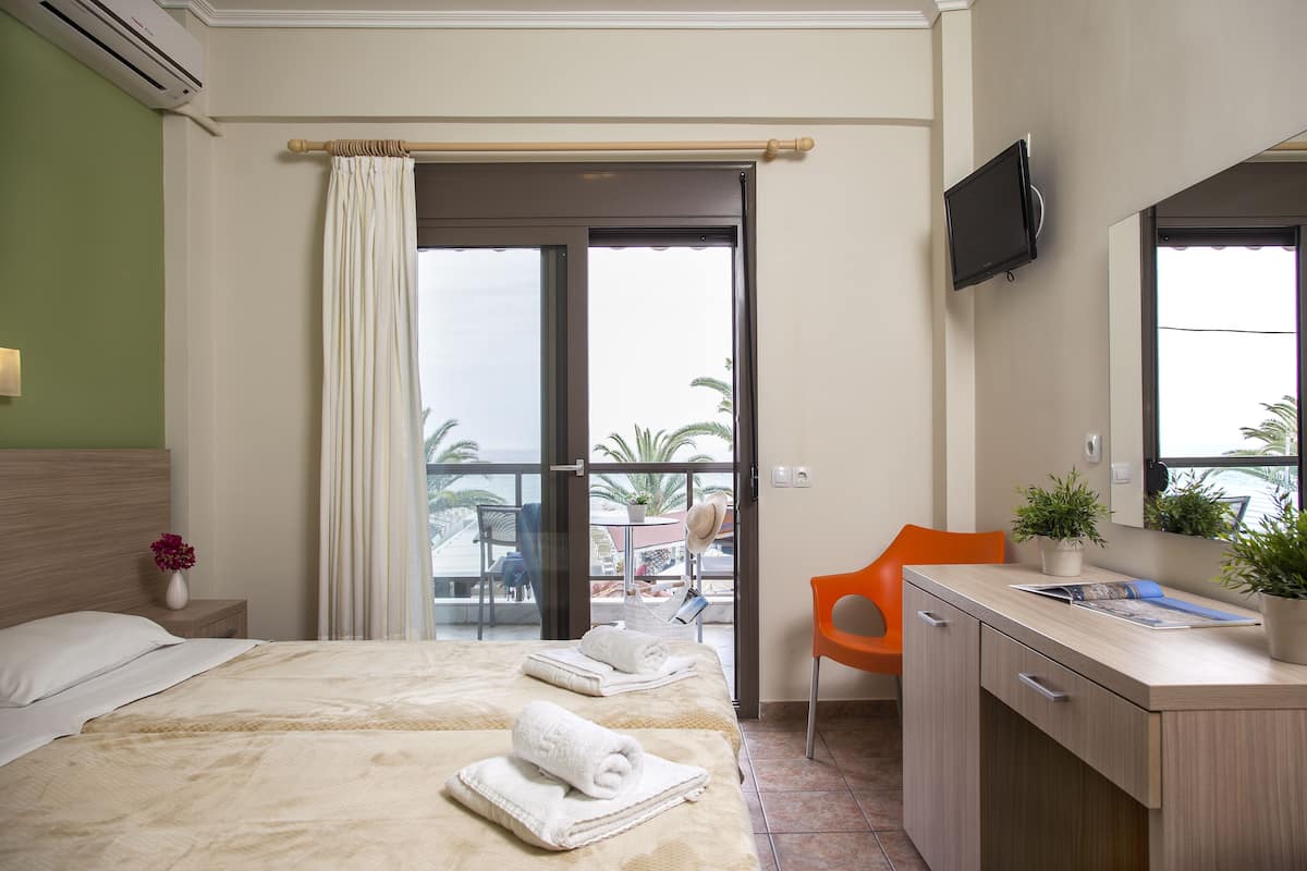 A hotel room with a bed, a desk, a chair, a TV, and a balcony with a view.