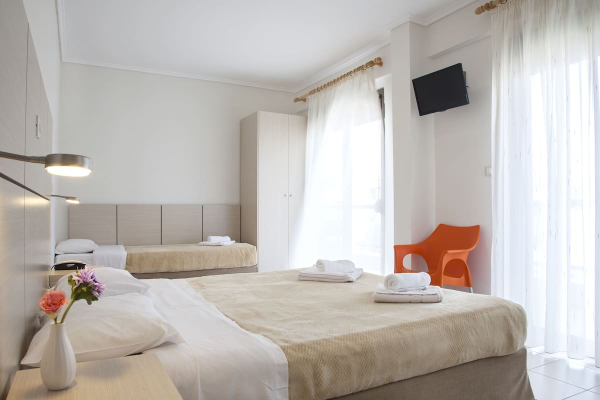 A hotel room with two beds, a TV mounted on the wall, and a window with sheer curtains.