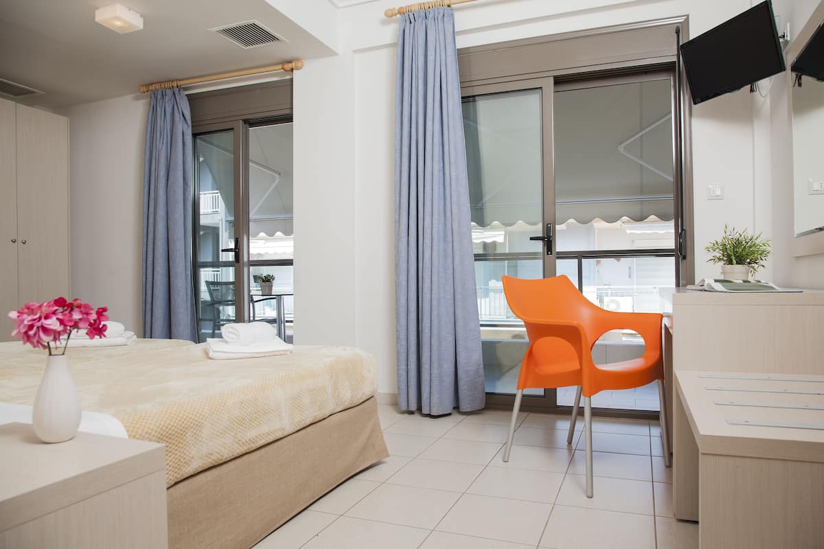 A hotel room with a bed, a desk, a chair, a TV, and a window with curtains.