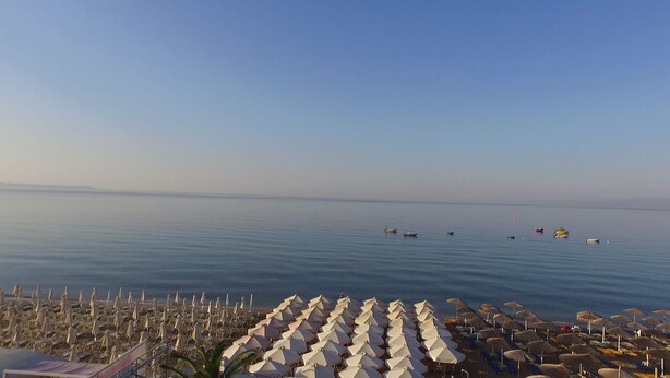 A beach with rows of umbrellas and lounge chairs, a calm sea, and a clear sky.