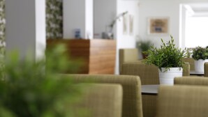 A modern dining area with a wooden reception desk, green plants, and comfortable seating.