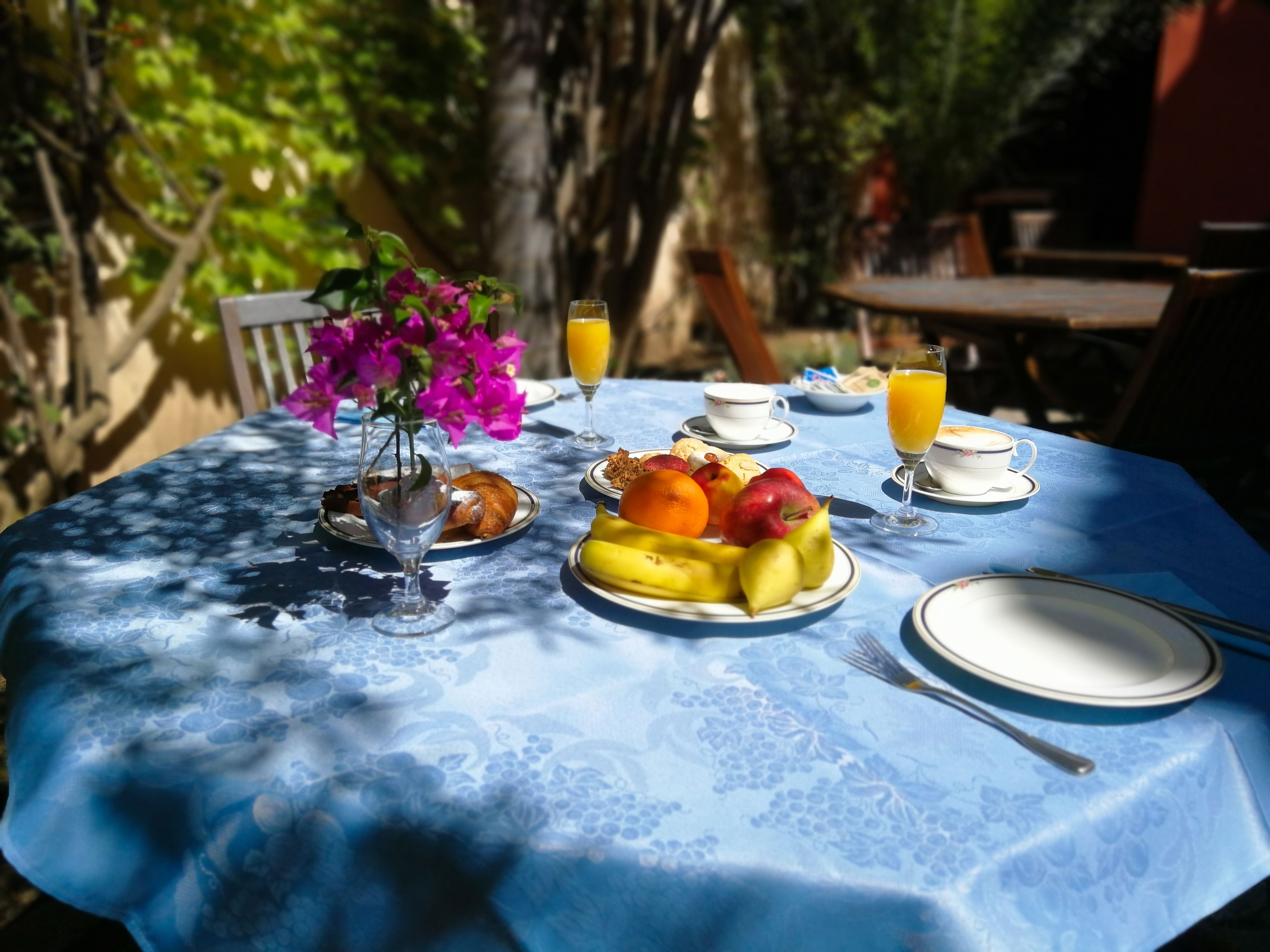 A table set with breakfast items including fruits, pastries, and beverages, surrounded by greenery.