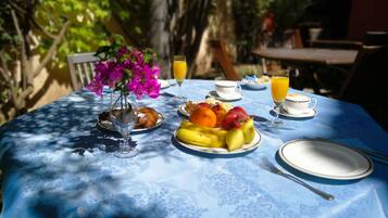 A table set with breakfast items including fruits, pastries, and beverages, surrounded by greenery.