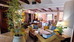 Una sala de estar acogedora con muebles de mimbre, una planta grande en maceta y un comedor al fondo.