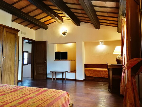 A hotel room with a bed, wooden ceiling beams, a television, a small table, and a bench.
