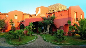 Un hotel de fachada roja, con varios arcos y un camino de grava que lleva a la entrada.