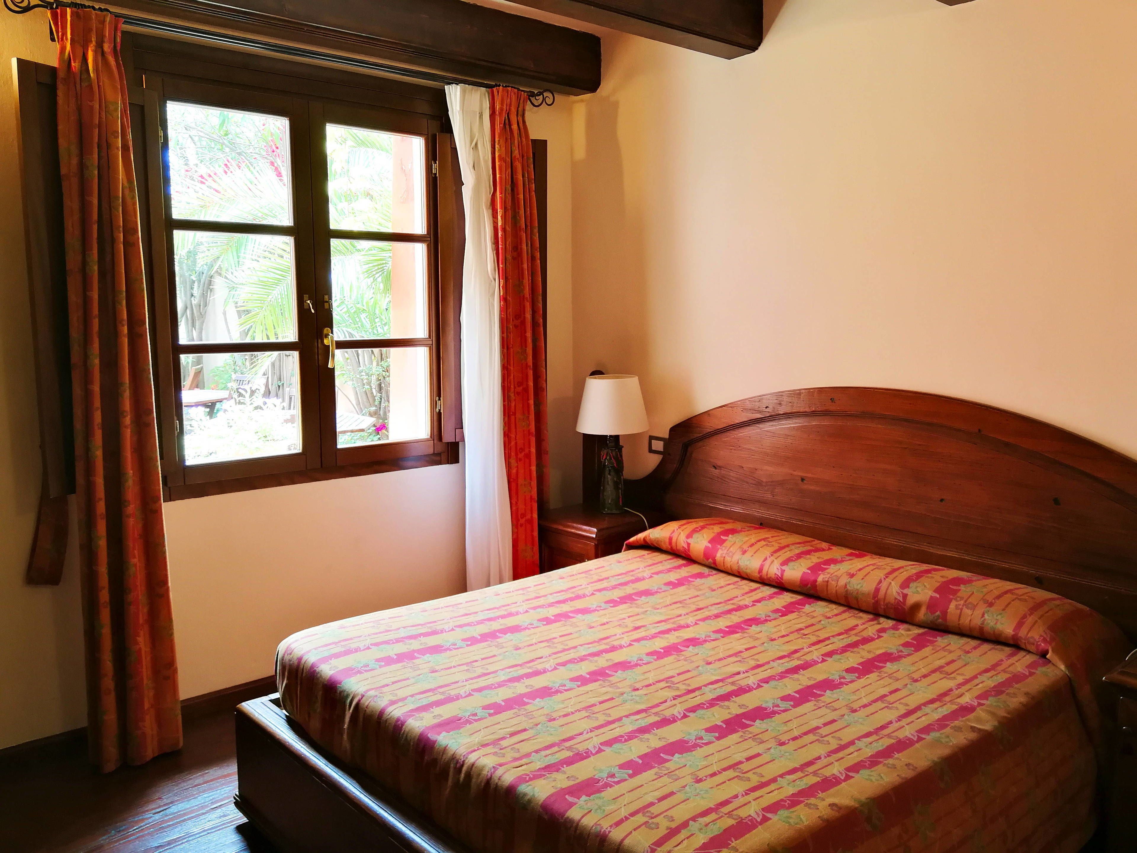 A bedroom with a bed, curtains, a window, and a nightstand with a lamp.