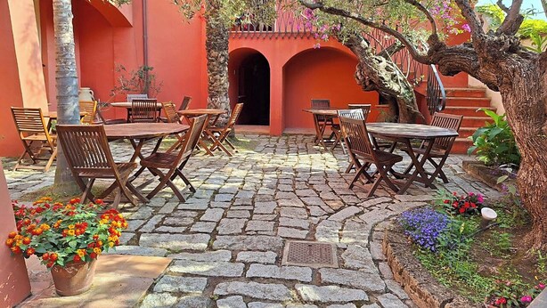 Un patio al aire libre con piso de piedra, mesas y sillas de madera, y plantas en macetas.