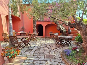 An outdoor patio with stone flooring, wooden tables and chairs, and potted plants.