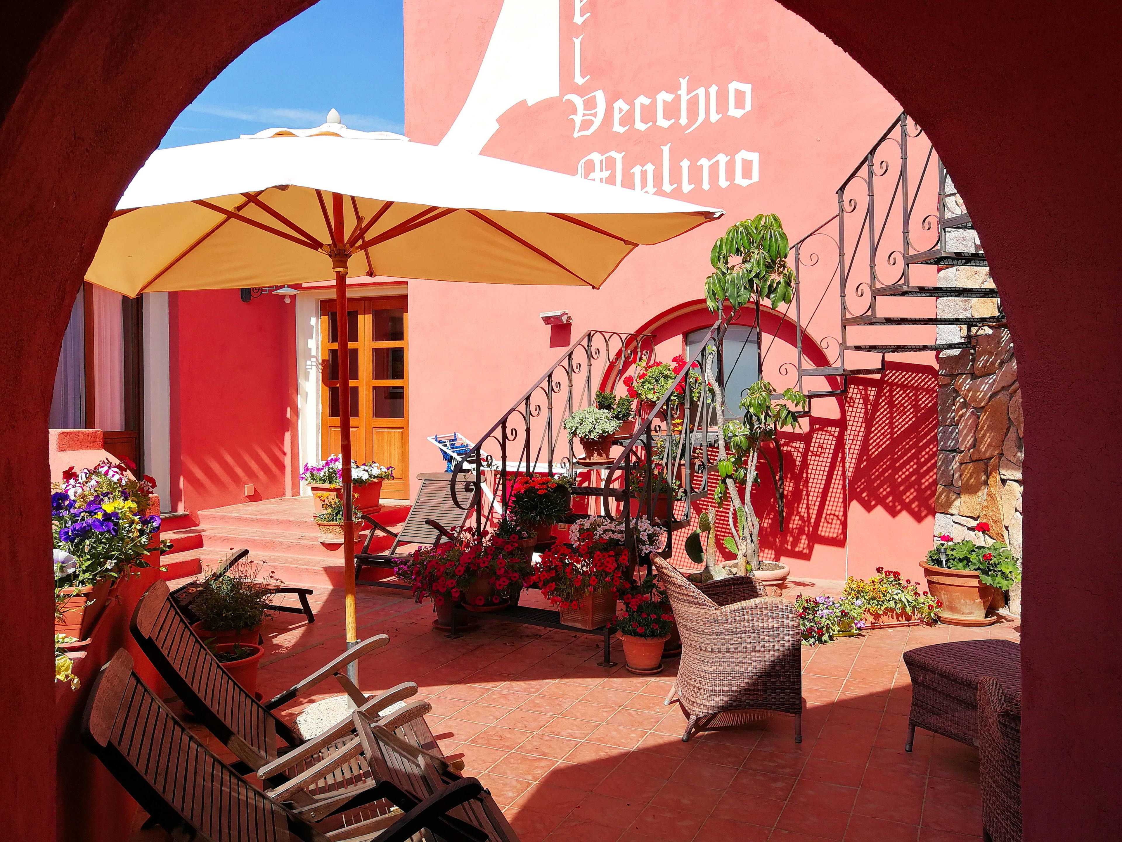 A courtyard with a red building, a wooden bench, a wicker chair, and potted plants.