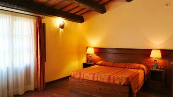 A hotel room with a wooden bed, two bedside tables with lamps, a wooden ceiling, and a window with sheer curtains.