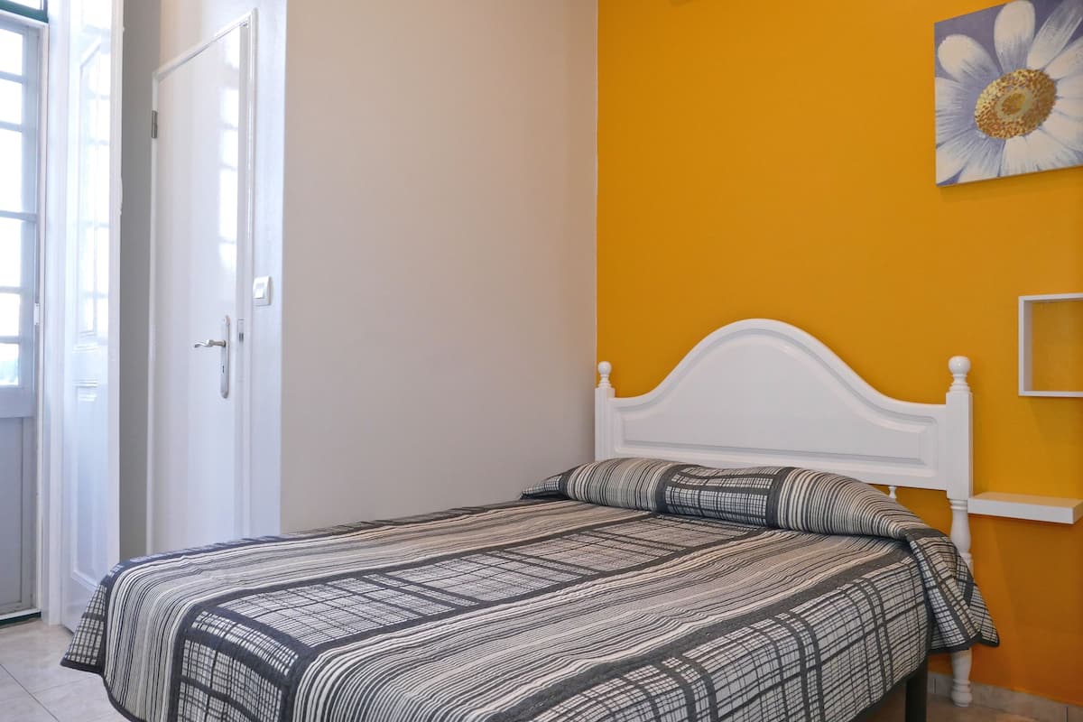 A bedroom with a white bed, a patterned bedspread, and a yellow wall.