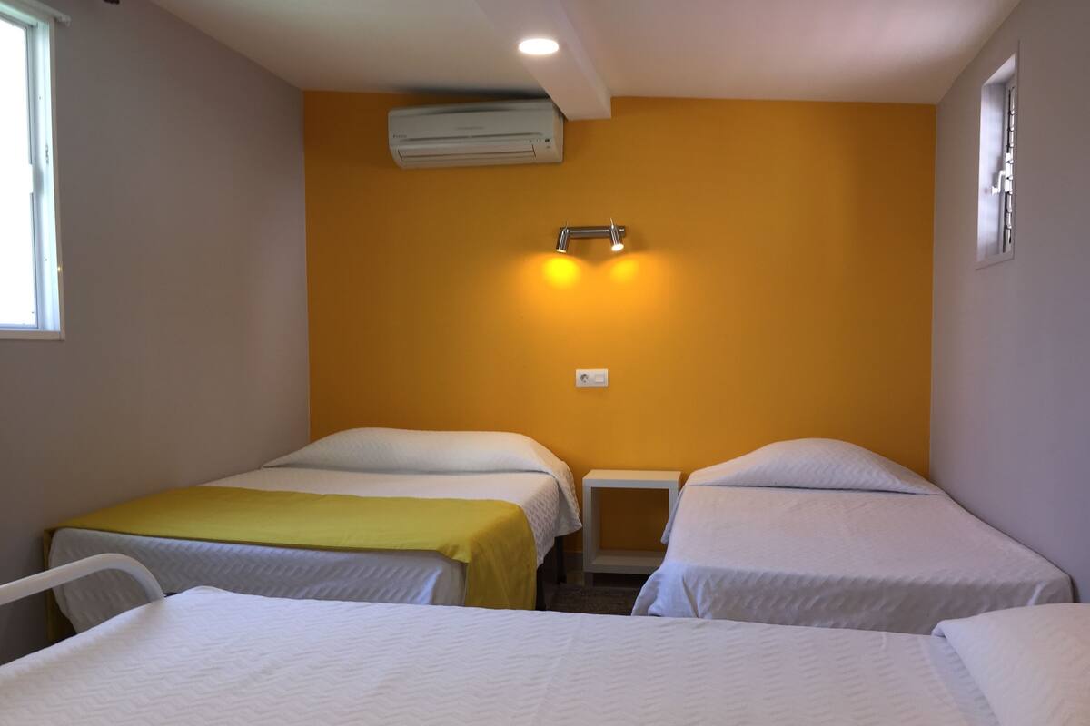 A room with two beds, a window, an air conditioning unit, and a wall-mounted light fixture.