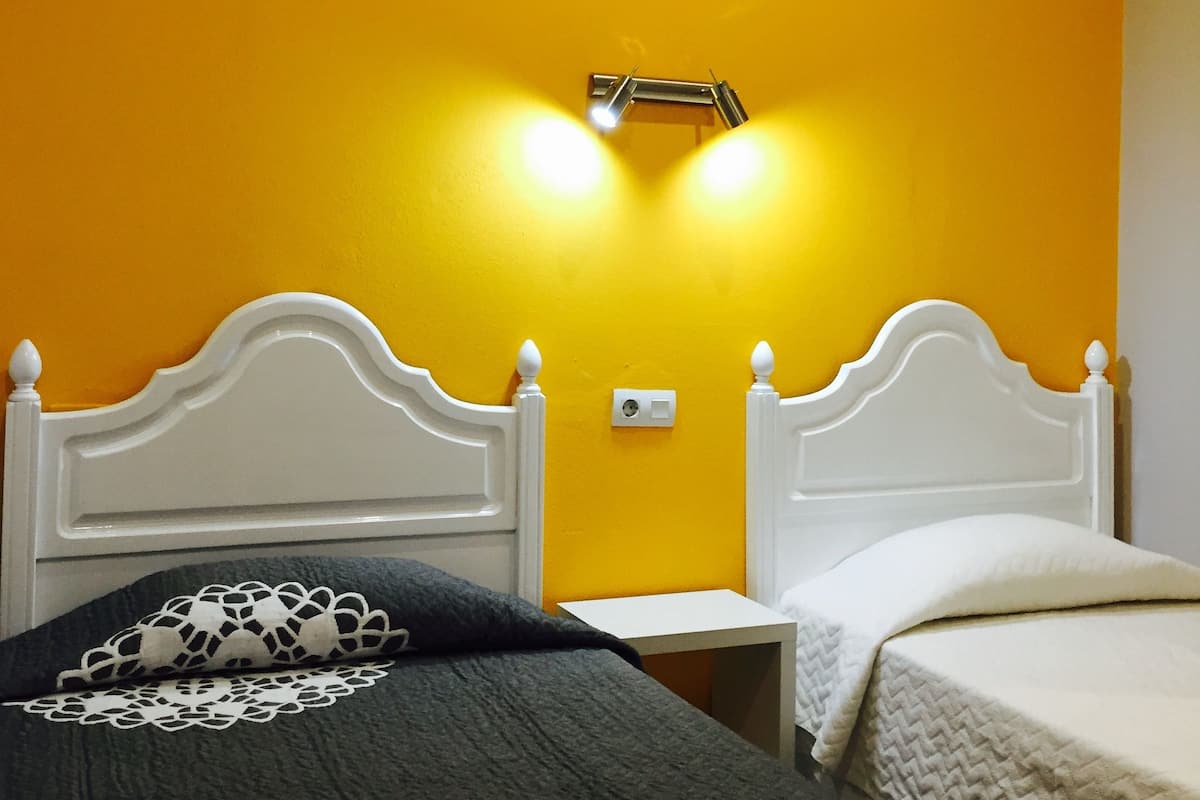 A room with two beds, a nightstand, an air conditioning unit, and a wall-mounted light fixture.