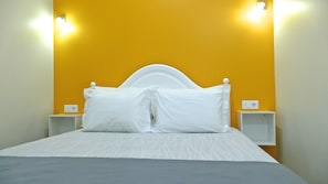 A bed with white bedding and pillows, two bedside tables, and a wall with a yellow accent. - Guest House São Filipe (Faro)