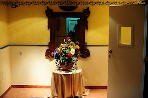 Un pasillo con una mesa redonda cubierta con un mantel color beige, un espejo en la pared y una puerta con un pequeño ventanal.