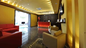 A hotel lobby with a reception desk, red and beige seating, and a large flat-screen TV on the wall. - Hotel Gabbiano (Manfredonia)
