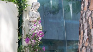 A statue of a woman with a child, surrounded by purple flowers, next to a glass window. - Hotel Gabbiano (Manfredonia)
