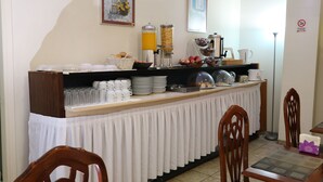 Una barra de desayuno con diversas opciones de comida, tazas y una máquina de café.