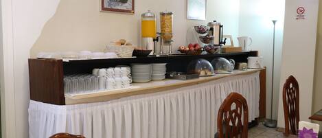A breakfast bar with various food items, cups, and a coffee machine.