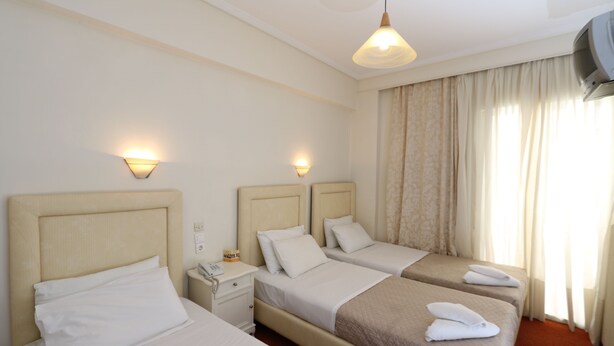 Habitación de hotel con tres camas, cada una con cabecera, mesitas de noche y lámparas.