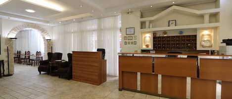 Un vestíbulo de hotel con mostrador de recepción, zona de estar y un reloj en la pared.