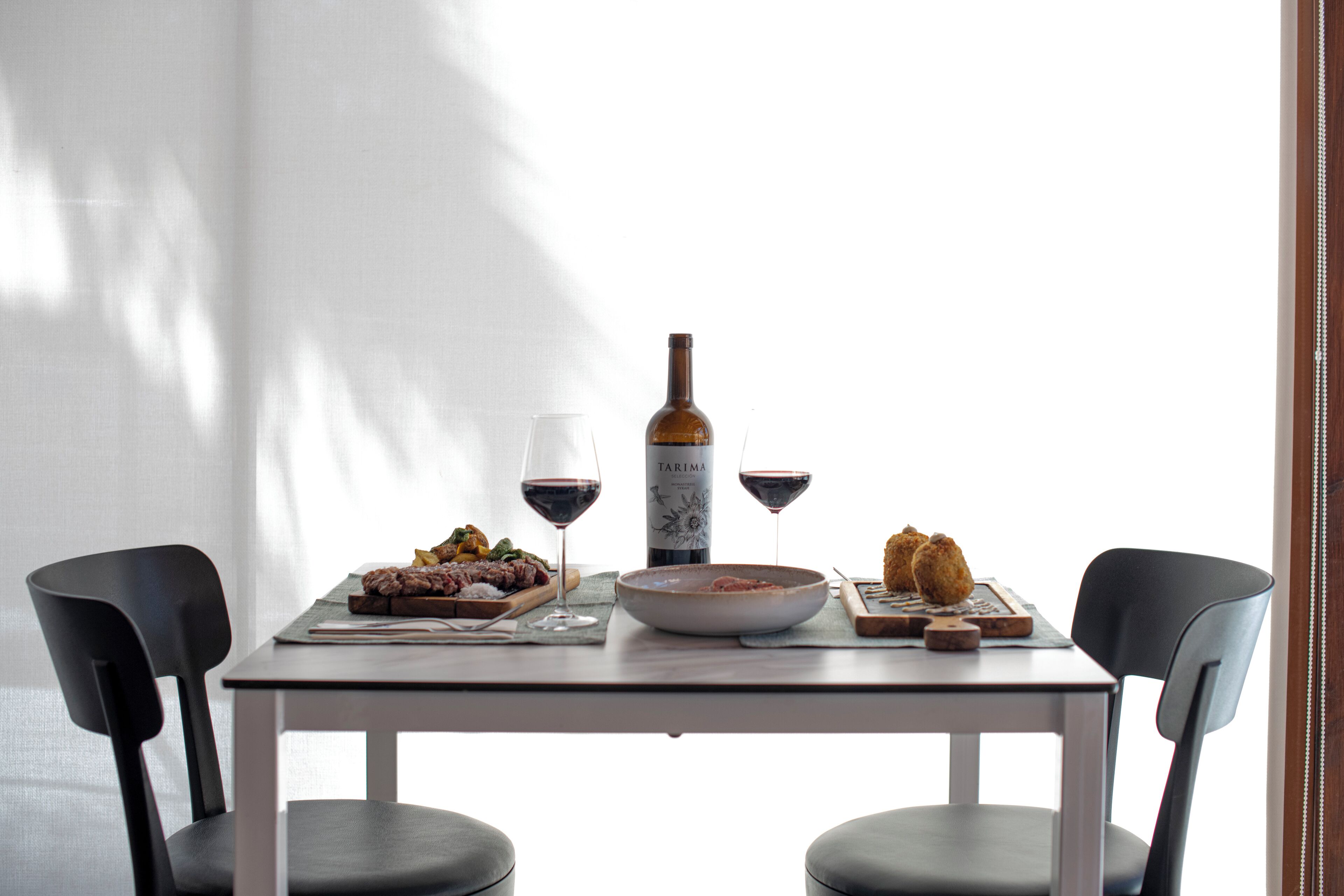 Une table à manger avec une bouteille de vin, des verres et une assiette de nourriture.
