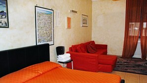 Habitación de hotel con dos camas, un sofá rojo, una mesita con una toalla y un mapa de la ciudad en la pared.
