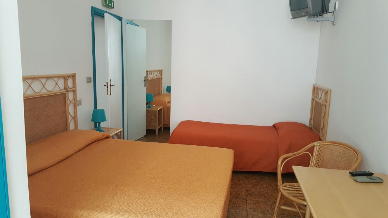 Een kamer met twee bedden, een bureau, een stoel, een televisie en een deur.