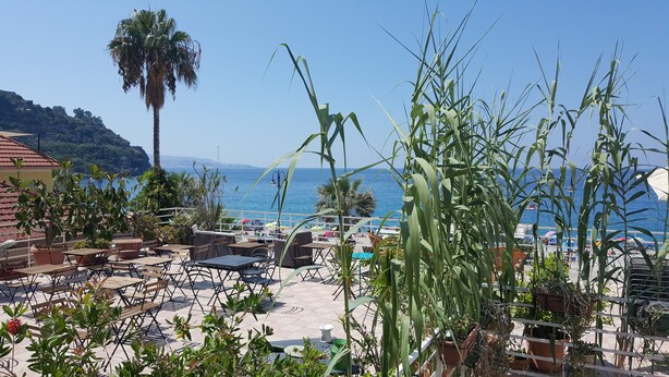 An outdoor seating area with tables and chairs, overlooking a beach and the sea. - Le Sirene Scilla (Scilla)