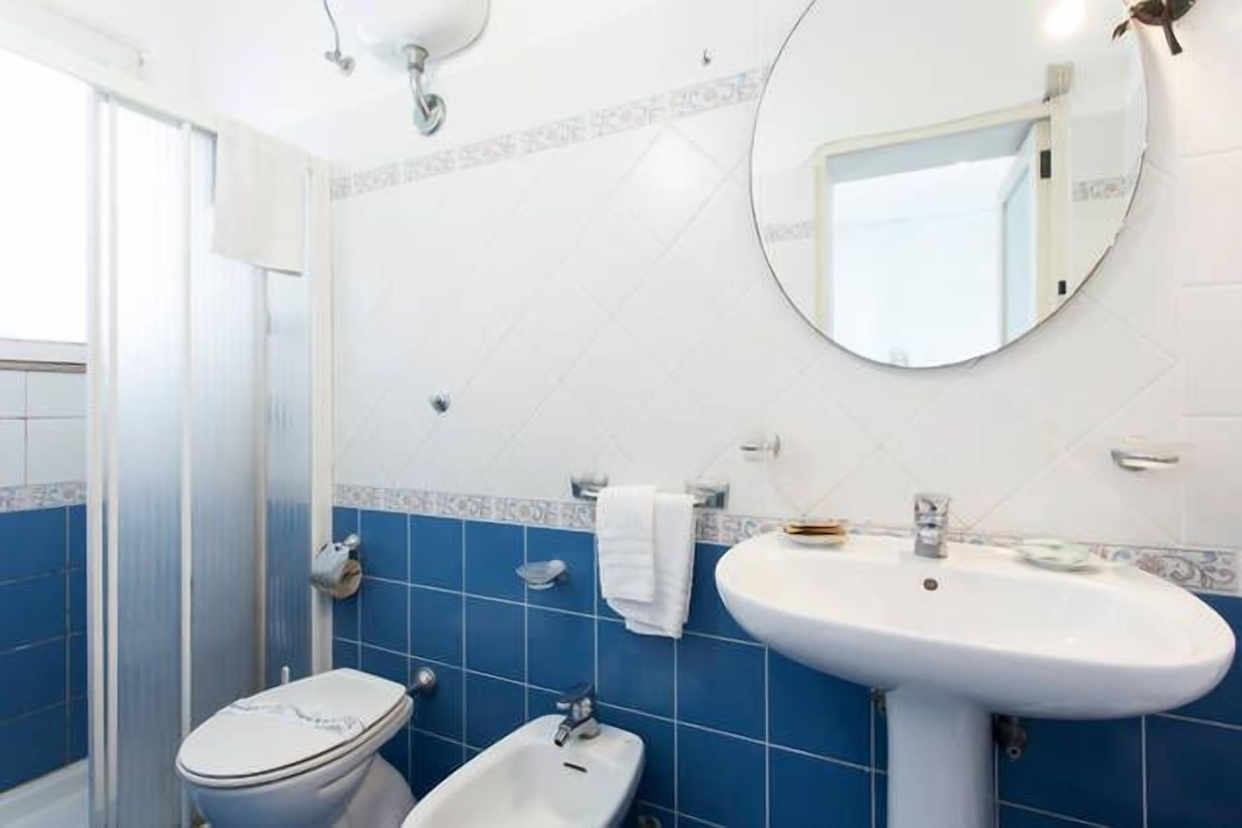 Un baño con inodoro, bidé y lavamanos, con azulejos azules y un espejo en la pared.