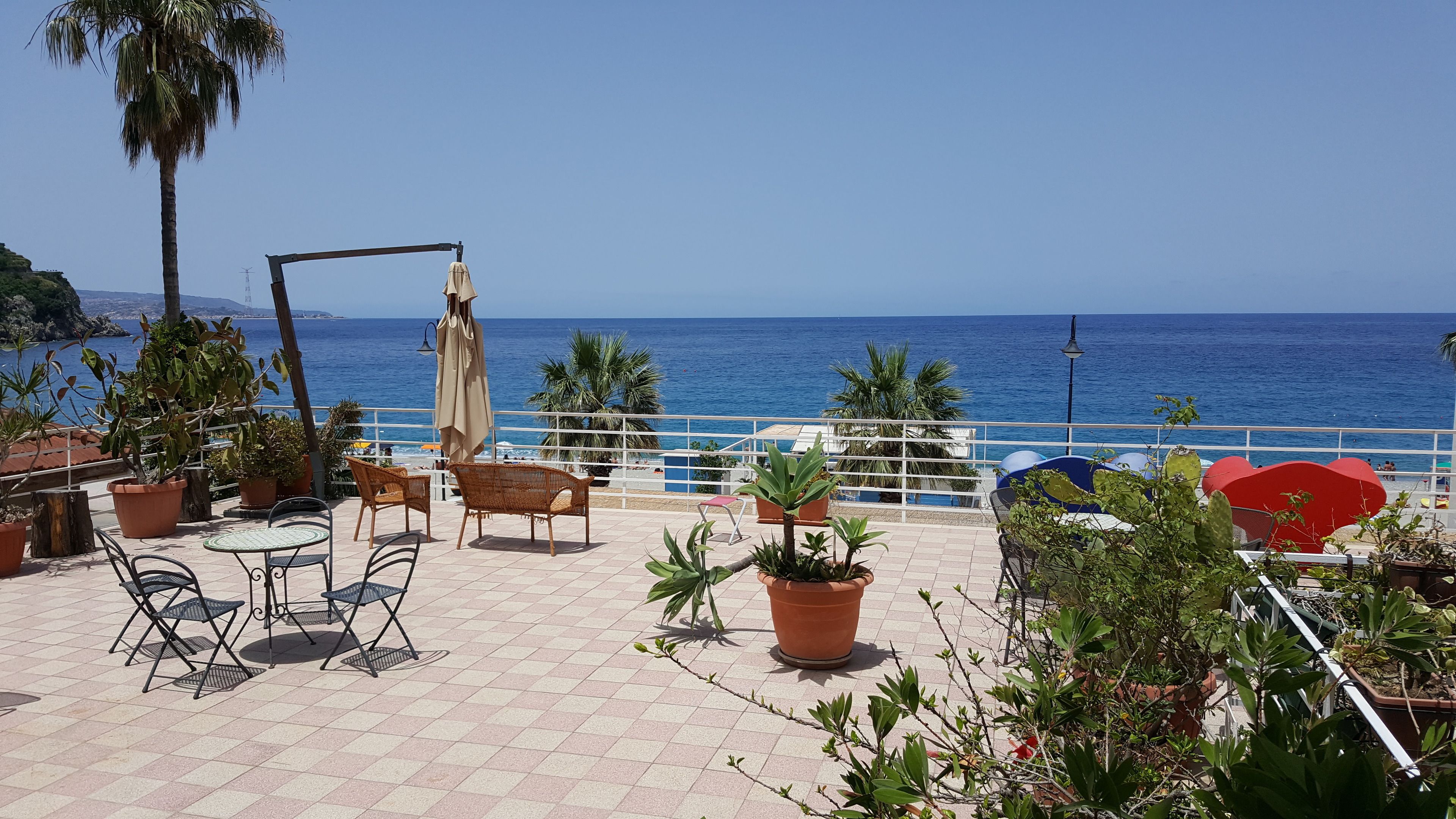 Une terrasse avec des chaises en osier, des plantes en pot et une vue sur la mer.
