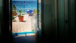 An open doorway leading to a balcony with a view of the sea, potted plants, and outdoor furniture. - Le Sirene Scilla (Scilla)