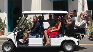 A white golf cart with passengers, parked in front of a building with a reception and a sign for Hotel Le Sirene. - Le Sirene Scilla (Scilla)