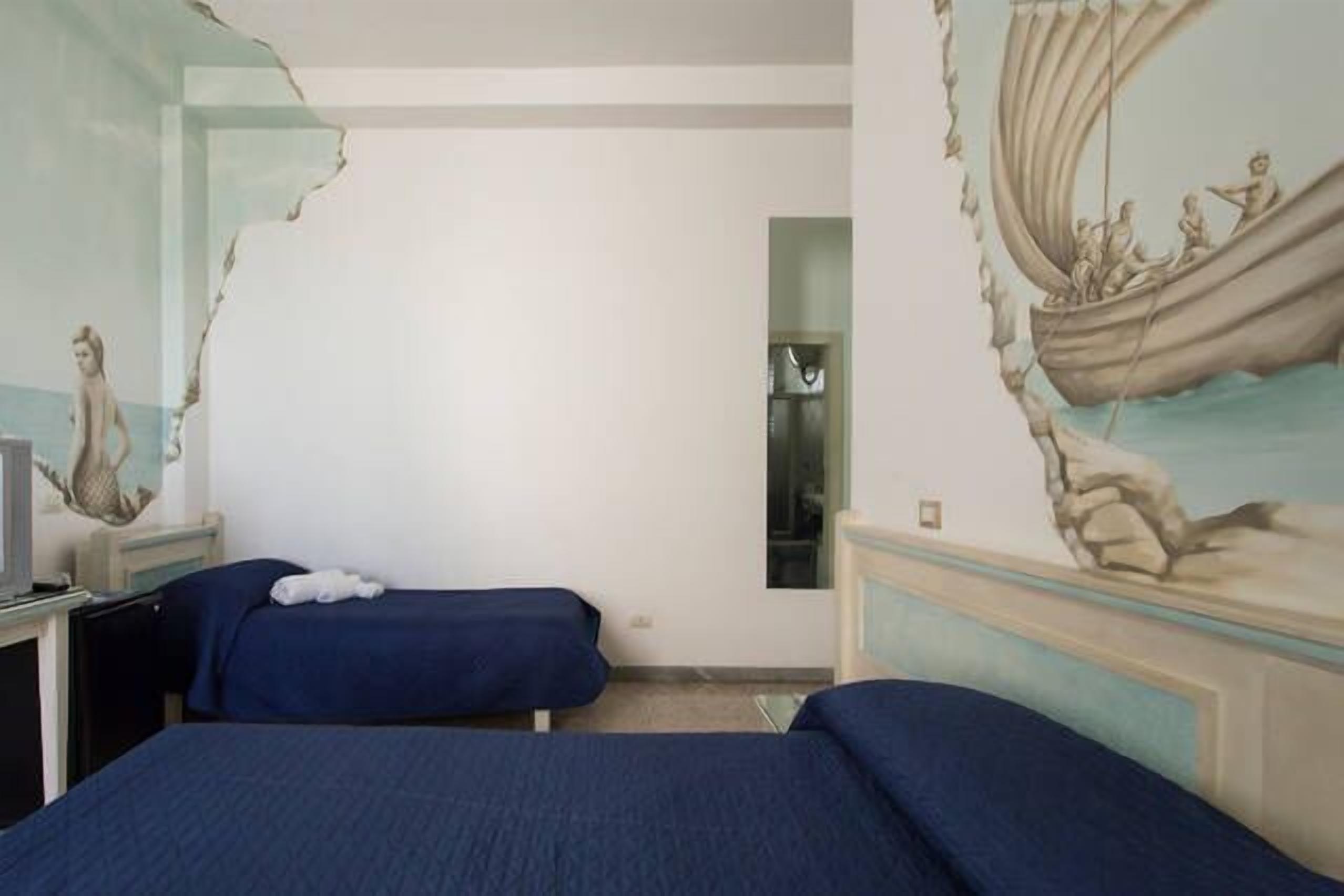 Una camera d'albergo con due letti, un murale raffigurante una nave a vela e una piccola scrivania con un televisore.
