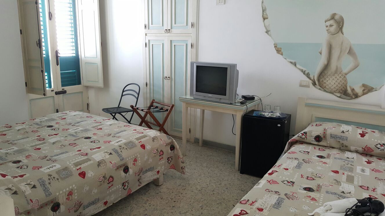 A bedroom with two beds, a desk with a television, a chair, and a small refrigerator.