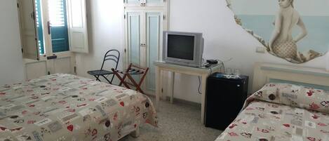 A bedroom with two beds, a desk with a television, a chair, and a small refrigerator.