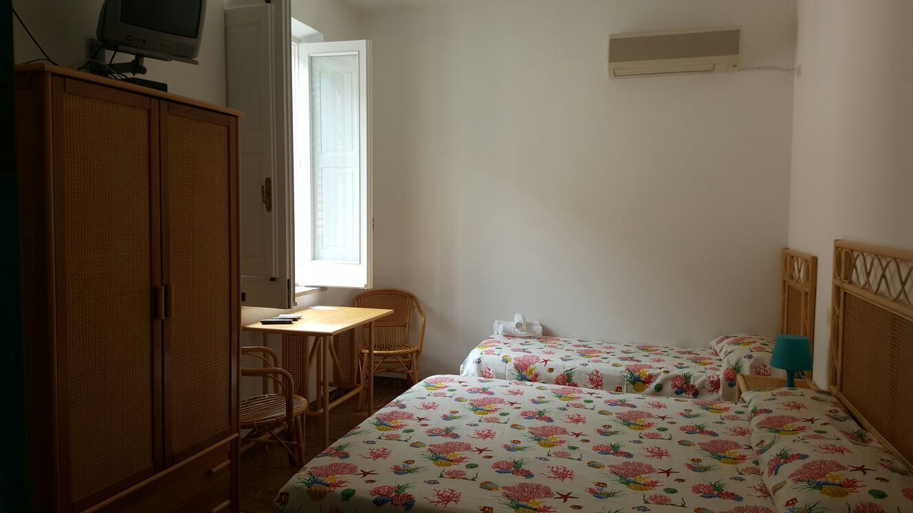 A room with two beds, a wooden wardrobe, a desk with a chair, and a television on a stand.