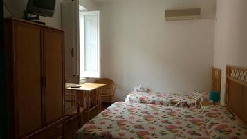 A room with two beds, a wooden wardrobe, a desk with a chair, and a television on a stand.