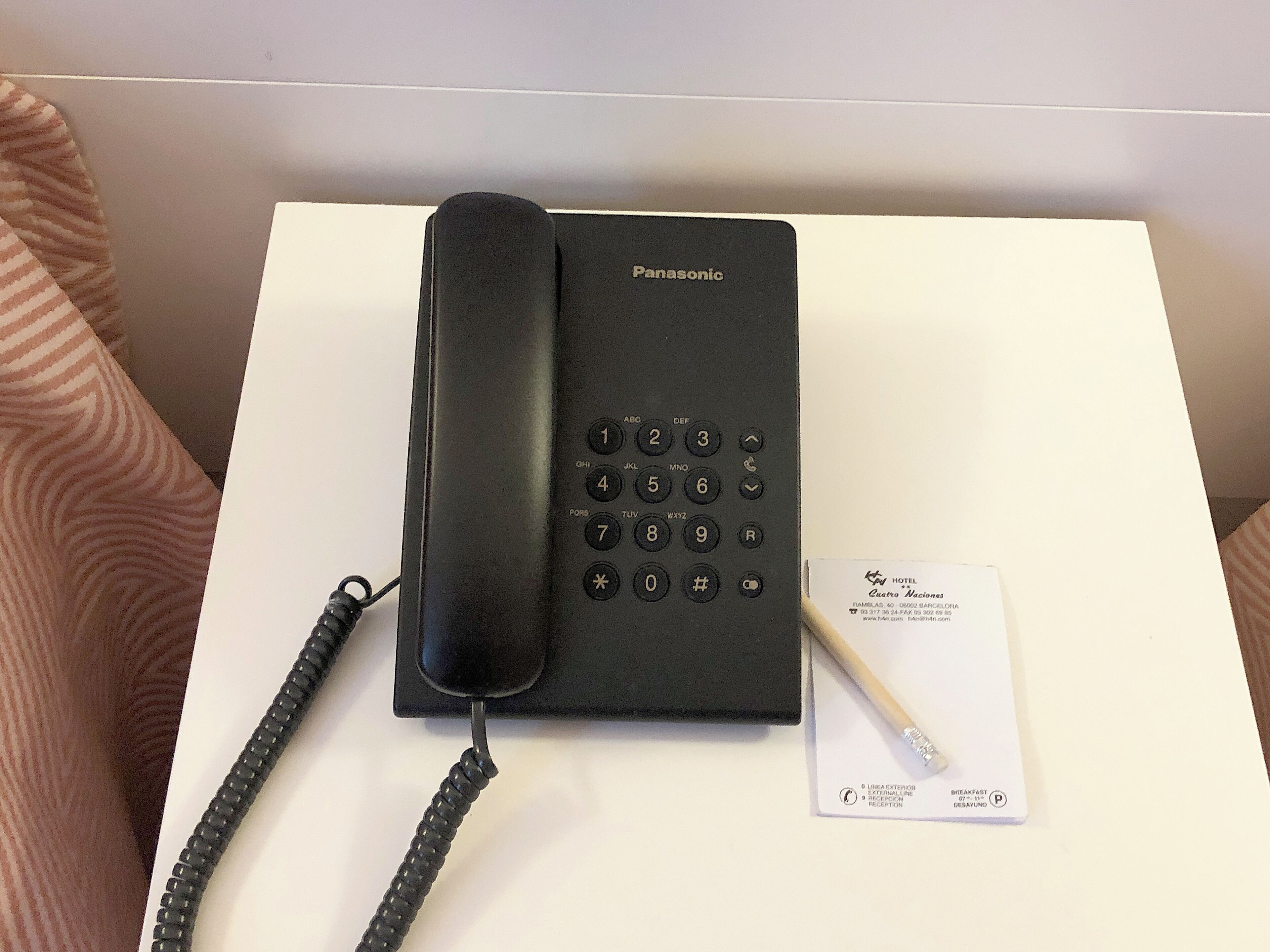 Un téléphone d’hôtel Panasonic posé sur une table blanche, avec une carte de visite et un stylo.