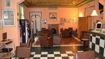 Eine Lobby mit Schachbrettboden, braunen Ledersesseln, einem Kamin und einer Bar mit Computer und Fernseher.