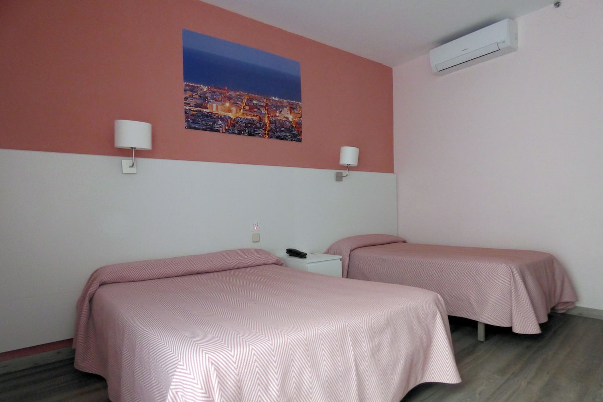 Une chambre d’hôtel avec deux lits, une table de chevet, une lampe et un tableau représentant un paysage urbain accroché au mur.