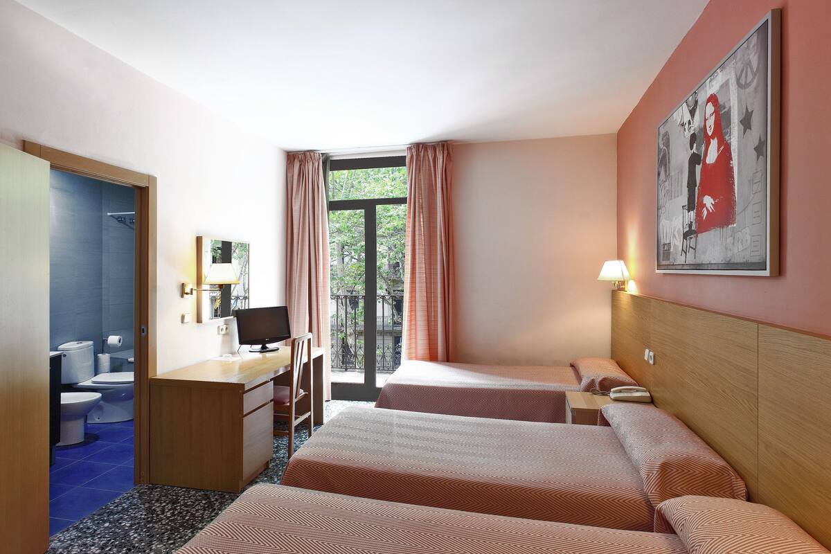 Une chambre d’hôtel avec deux lits, un bureau avec un ordinateur, une chaise et une fenêtre avec des rideaux.